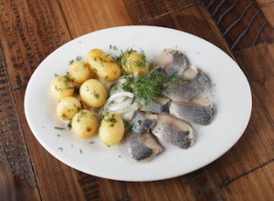 Herring fish with young potato on white plate. wooden background.